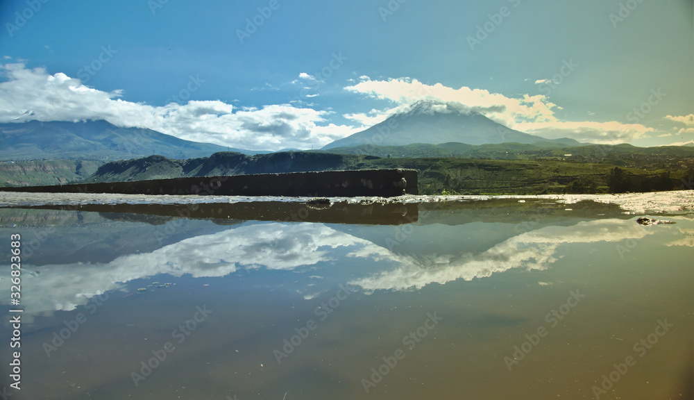 The misti volcano in the city of Arequipa, with clouds and snow on its summit, reflected in a puddle of water from a rural road, the scene shows the blue sky, early in the morning.
