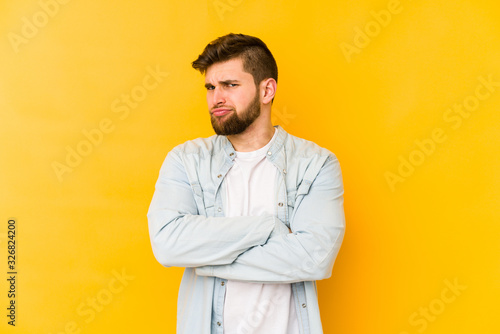 Young caucasian man isolated on yellow background suspicious, uncertain, examining you.