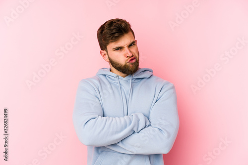 Young caucasian man isolated on pink background frowning face in displeasure, keeps arms folded.