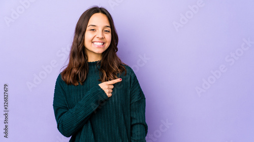 Young mixed race hispanic woman isolated smiling and pointing aside, showing something at blank space. © Asier