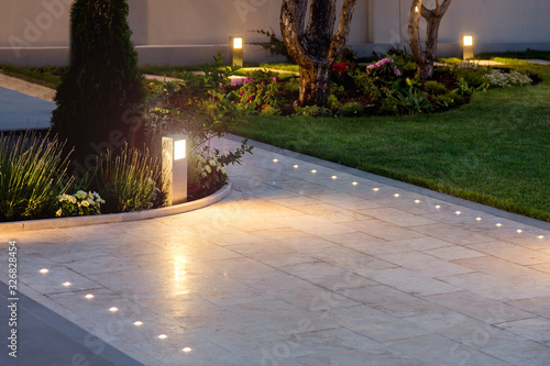 marble tile playground in the night backyard of mansion with flowerbeds and lawn with ground lamp and lighting in the warm light at dusk in the evening.