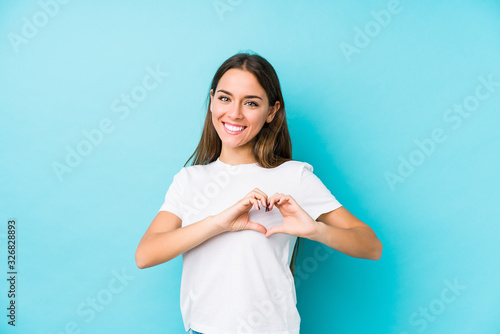 Young caucasian woman  isolated smiling and showing a heart shape with hands.
