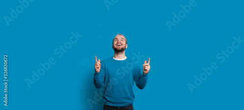 Fotografija Blonde caucasian man with nice beard is pointing and looking up to the blue free