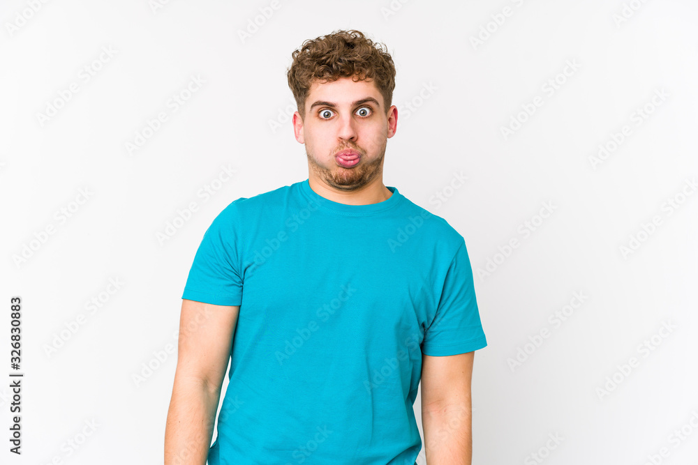 Obraz premium Young blond curly hair caucasian man isolated blows cheeks, has tired expression. Facial expression concept.