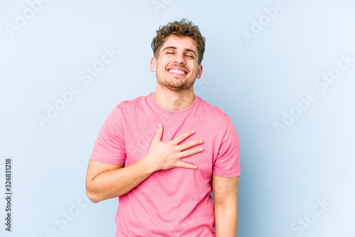 Young blond curly hair caucasian man isolated laughs out loudly keeping hand on chest.