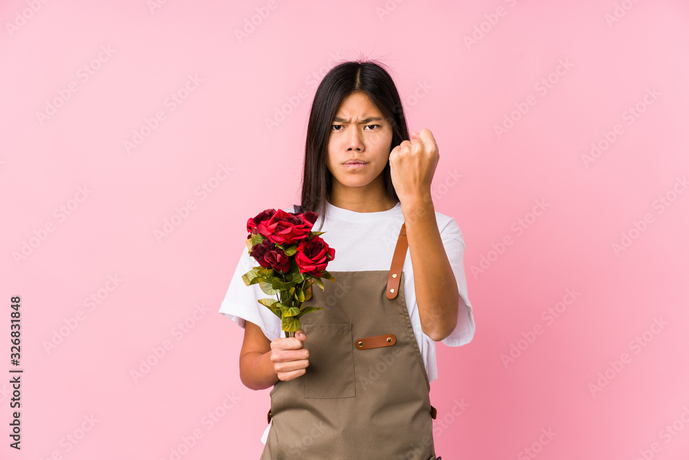 Young chinese gardener woman holding a roses isolated showing fist to camera, aggressive facial expression. Young chinese gardener woman holding a roses isolated showing fist to camera, aggressive facial expression.