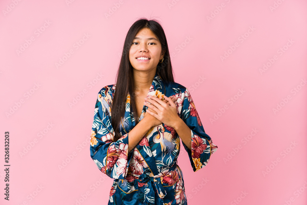Young asian woman wearing a kimono pajamas has friendly expression, pressing palm to chest. Love concept. Young asian woman wearing a kimono pajamas has friendly expression, pressing palm to chest. Love concept.