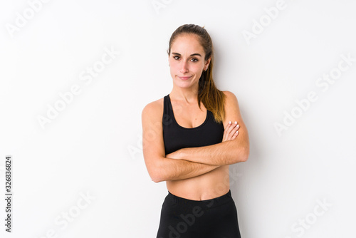 Young caucasian fitness woman posing in a white background frowning face in displeasure, keeps arms folded.