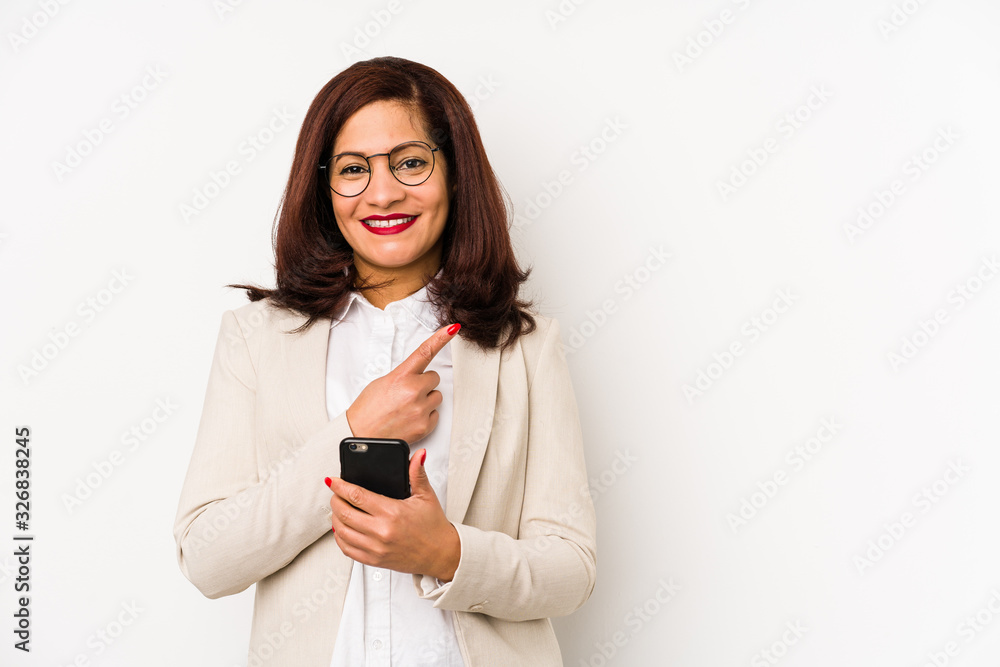 Middle age latin woman holding a mobile phone isolated smiling and pointing aside, showing something at blank space. Middle age latin woman holding a mobile phone isolated smiling and pointing aside, showing something at blank space.