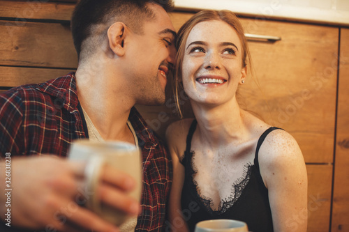 Charming red haired girl with freckles drinking a coffee in the mooring near her caucasian lover in the kitchen on the floor photo