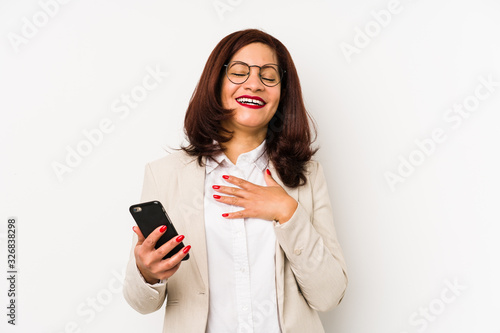 Middle age latin woman holding a mobile phone isolated laughs out loudly keeping hand on chest.
