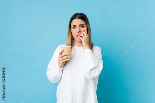 Young caucasian woman holding a takeaway coffee biting fingernails, nervous and very anxious.