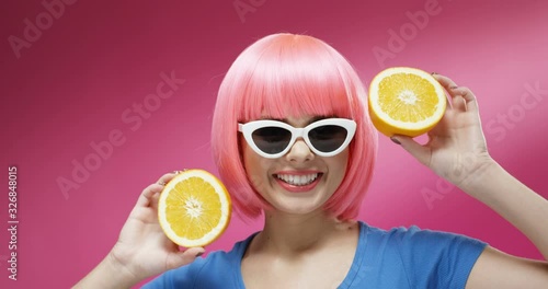 Wallpaper Mural Close up of pretty Caucasian young woman in sunglasses and pink wig closing eyes with two halves of orange and smiling cheerfully. Portrait of beautiful happy girl playing with fruit and dancing. Torontodigital.ca