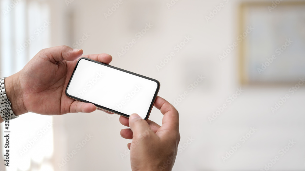 Close up view of businessman holding horizontal smartphone in simple office room Close up view of businessman holding horizontal smartphone in simple office room