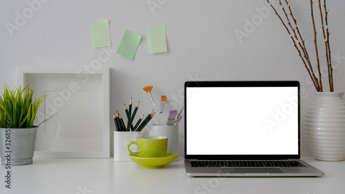 Close up view of workplace with blank screen laptop, stationery, green cup and decorations on white table © bongkarn