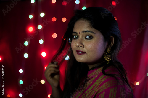 Close up portrait of an Indian Bengali beautiful brunette woman in front of the colorful light bokeh background created by tiny chain lights  in the evening of Diwali. Indian lifestyle and religion.