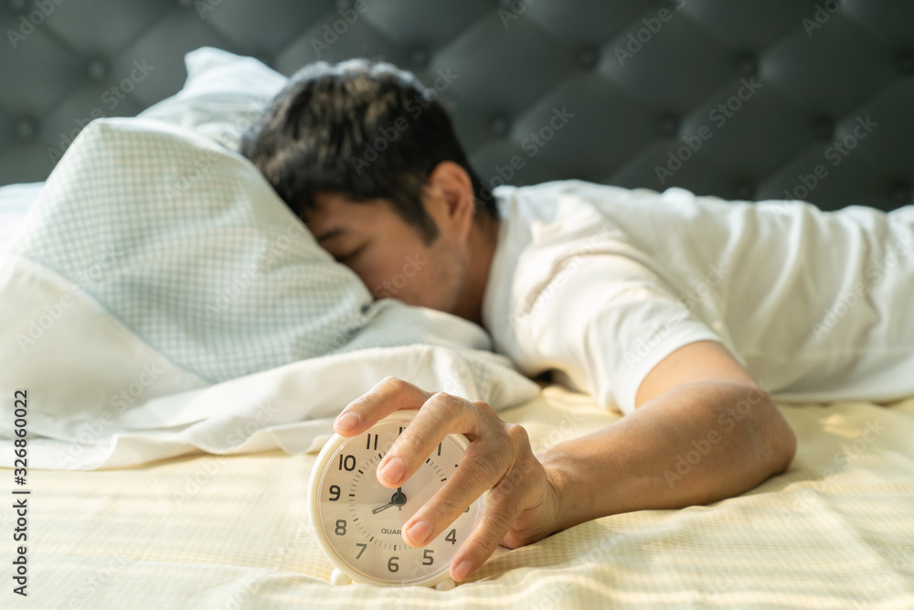 Asian man  wake up in the morning and hand reaching alarm clock - obrazy, fototapety, plakaty 