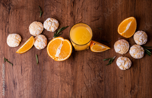 Shortbread orange biscuits with sprigs of semarin, with fresh orange and juice on the table.