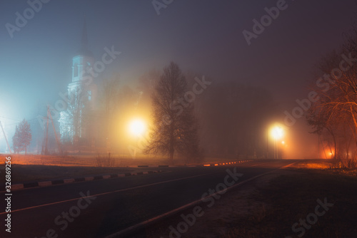 empty street in the fog at night by the light of lanterns, the church is visible through the fog
