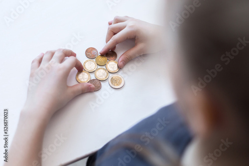 A little girl's hands count Euro coins. The child saves money on the concept of the future