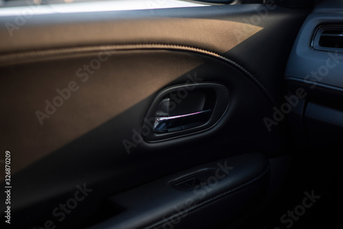 Inner car door handle of a compact modern car, view from an interior of a back seat. Seeing inside car door decorated with dark leather and chrome. Nice sun rise shining in a parking lot.