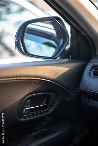 Folded wing mirror of a compact modern car, with a side window glass drop down for ventilation, seeing an inner car door handle. Car parked in a parking lot during the morning time with sun rise.