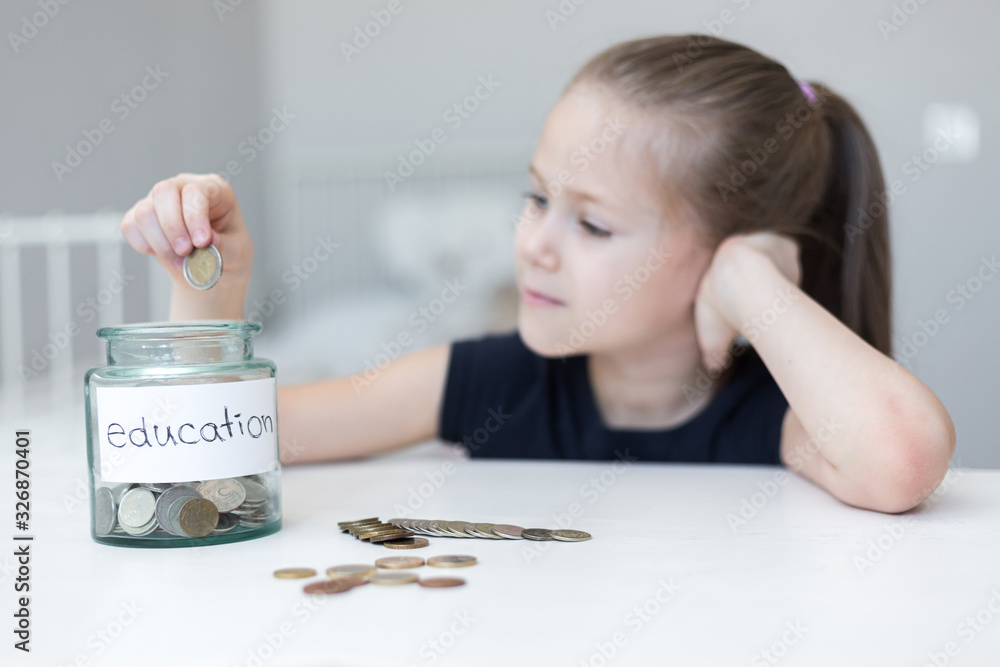 A little girl saves money for education. child counts and puts coins in a glass bottle in her room. The child saves money on the concept of the future A little girl saves money for education. child counts and puts coins in a glass bottle in her room. The child saves money on the concept of the future
