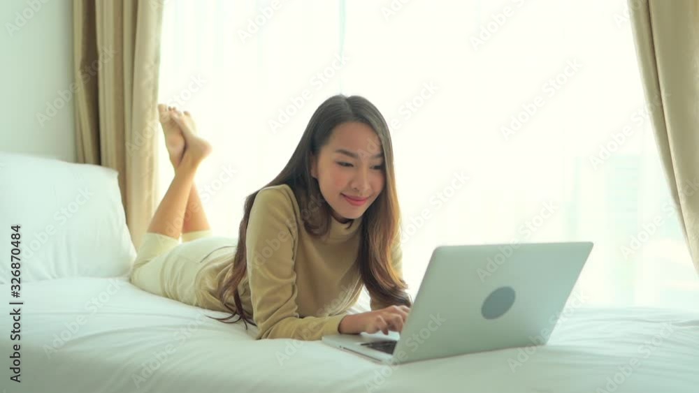 A pretty young woman works on her laptop while lying on the bed in her hotel room. A pretty young woman works on her laptop while lying on the bed in her hotel room.