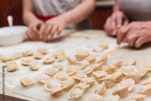 Little girl with grandmother in the kitchen sculpts dumplings