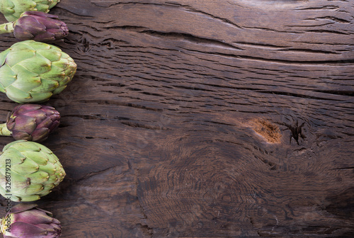 Green and purple artichoke flower edible buds on wooden background. photo