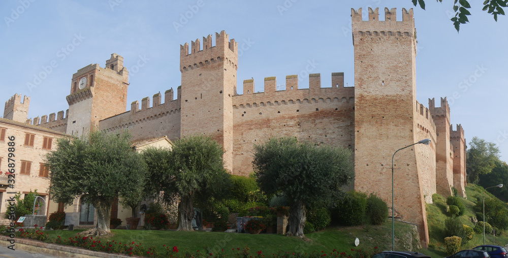 External walls with towers and laces around the village of Gradara with olive trees and green lawn.