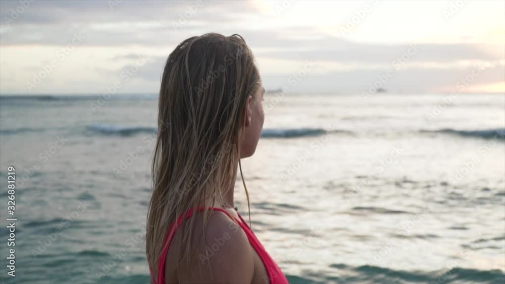 Beautiful Girl in Red Swimsuit walks out into ocean during sunset and lightly runs her harnds through the water in Hawaii.mp4