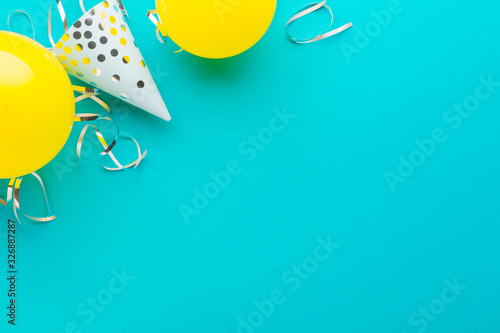 Blue caps, blue and yellow balloons and silver serpentine on a blue paper background. Holiday background. Copy space