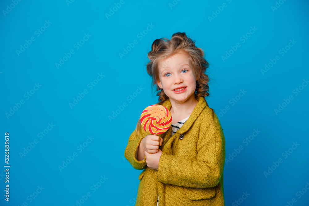 portrait of a baby girl in a coat holding a Lollipop on a colored blue background portrait of a baby girl in a coat holding a Lollipop on a colored blue background