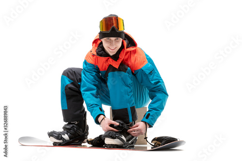 Portrait young man in sportswear with snowboard fastens boots isolated white background