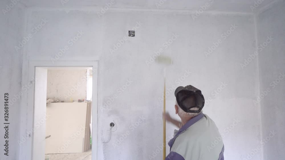 Back view of a senior painter painting wall with roller. Back view of a senior painter painting wall with roller.