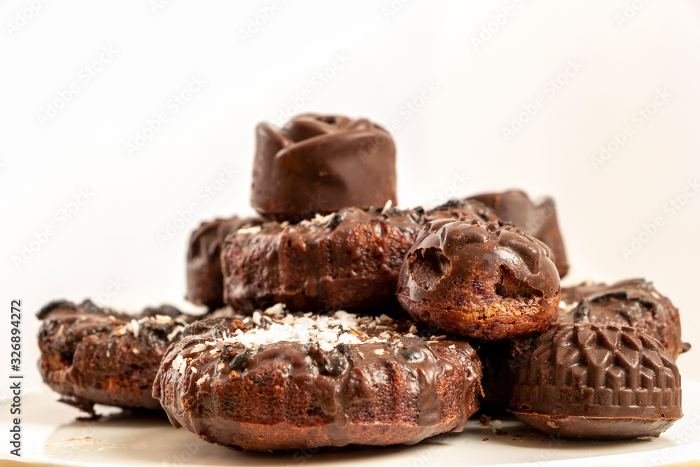 Delicious chocolate dietary treats for vegans made from natural ingredients. Candy and raisin cookies, sprinkled with coconut, on a white plate. Light background with place for text. Selective focus