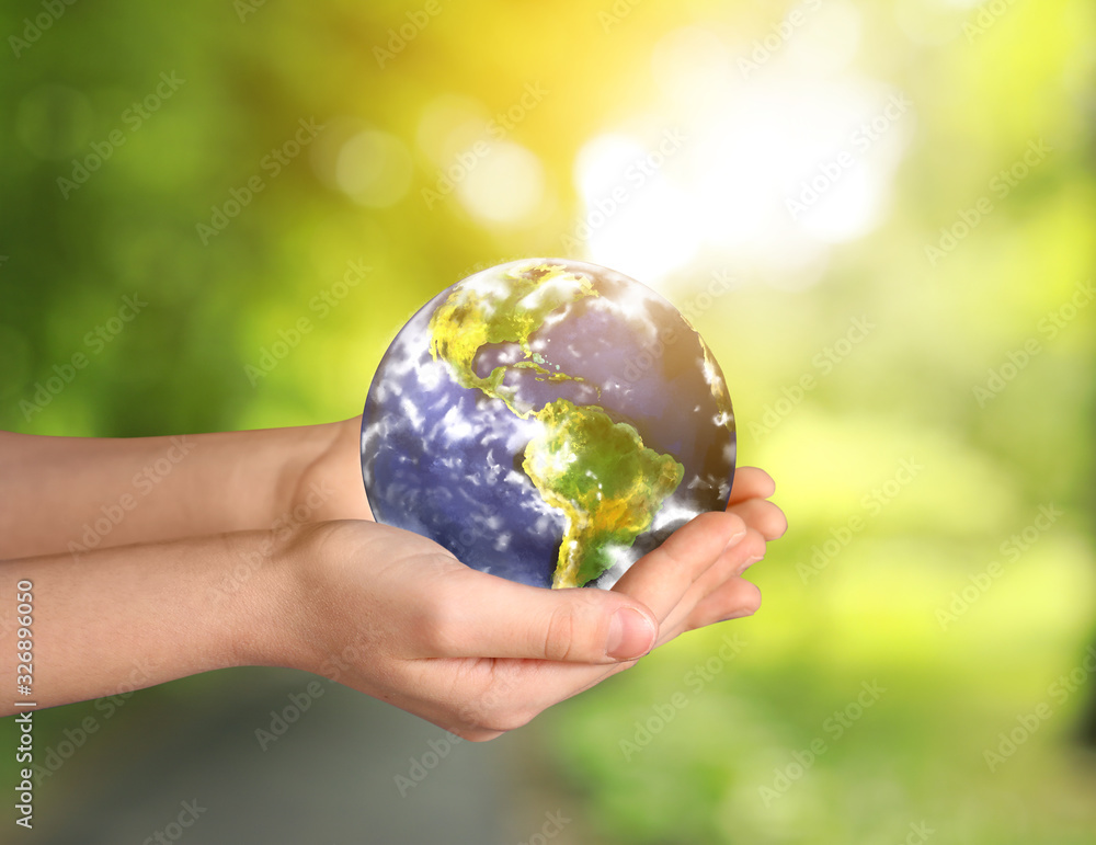 Hands of little child with planet on blurred background. Earth Day celebration