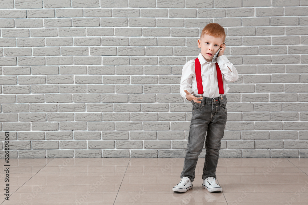 Stylish little boy talking by mobile phone near grey wall Stylish little boy talking by mobile phone near grey wall