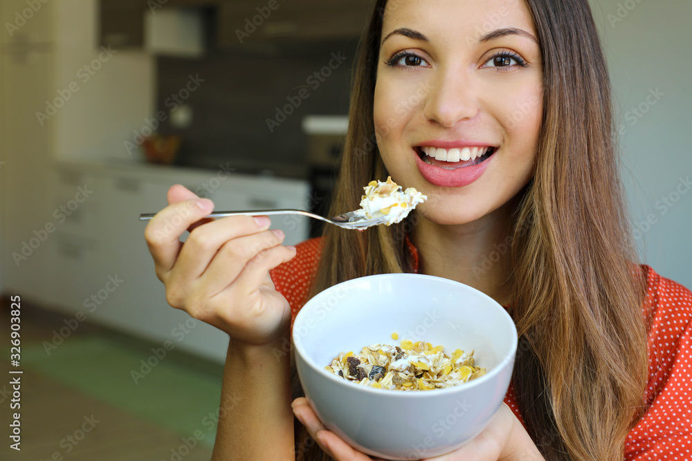 Close up of beautiful young woman eating skyr yogurt with cereal muesli fruit at home, looking at camera, focus on the model eyes, indoor picture. Healthy breakfast concept. Close up of beautiful young woman eating skyr yogurt with cereal muesli fruit at home, looking at camera, focus on the model eyes, indoor picture. Healthy breakfast concept.