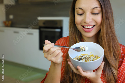 Close up of beautiful young woman eating skyr yougurt with cereal muesli fruit at home  focus on the model eyes  indoor picture. Healthy food concept.