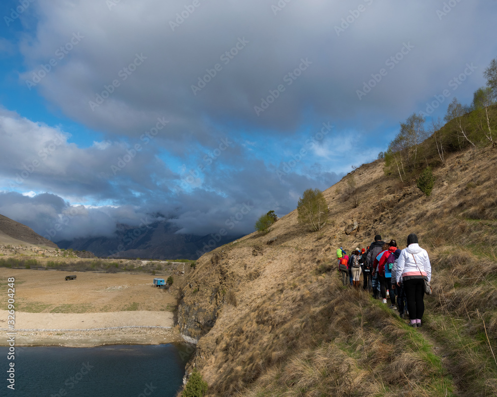 Bylym village, Kabardino-Balkarian Rep, Russia, 03/03/2019 a group of tourists walking along a trail next to a lake surrounded by mountains.