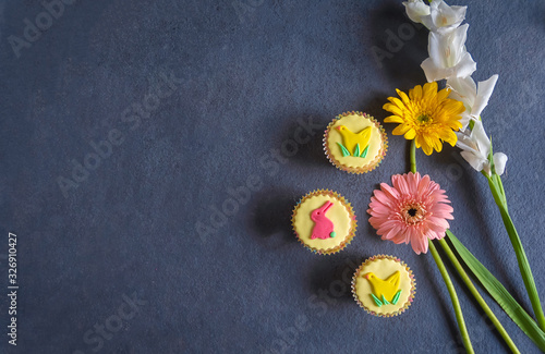 Pretty yellow vegan Easter cupcakes with colorful pastel icing shapes of Easter bunny rabbits, chicks together with Easter flowers