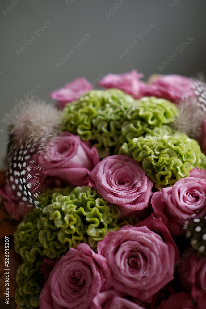Beautiful spring bouquet close-up with pink roses and green carnations, decorated with feathers and birch bark. 