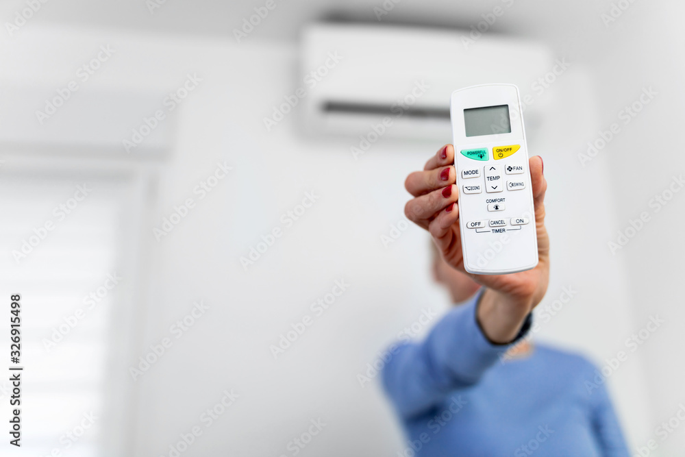 Woman holding a remote of a modern airconditioner unit at home. Woman holding a remote of a modern airconditioner unit at home.