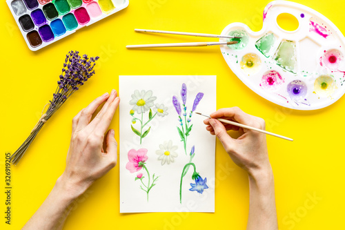 Painting. Female hands draw flowers on yellow background top-down