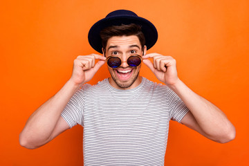Photo of attractive crazy funky youngster guy taking off cool eyeglasses see advert banner wear retro hat sun specs striped t-shirt isolated bright orange color background