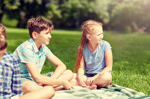 friendship, childhood, leisure and people concept - group of happy kids or friends sitting on grass in summer park