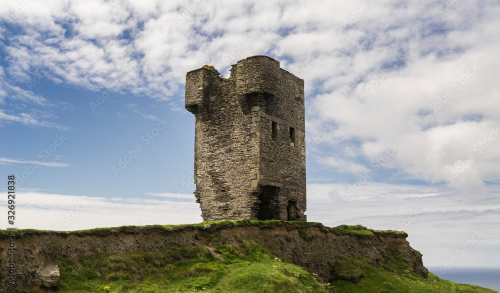 Ruins of an ancient tower on the cliffs of Moher in Ireland with the sea in the background and cloudy skies.