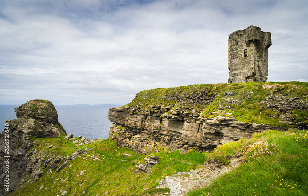 Ruins of an ancient tower on the cliffs of Moher in Ireland with the sea in the background and cloudy skies.